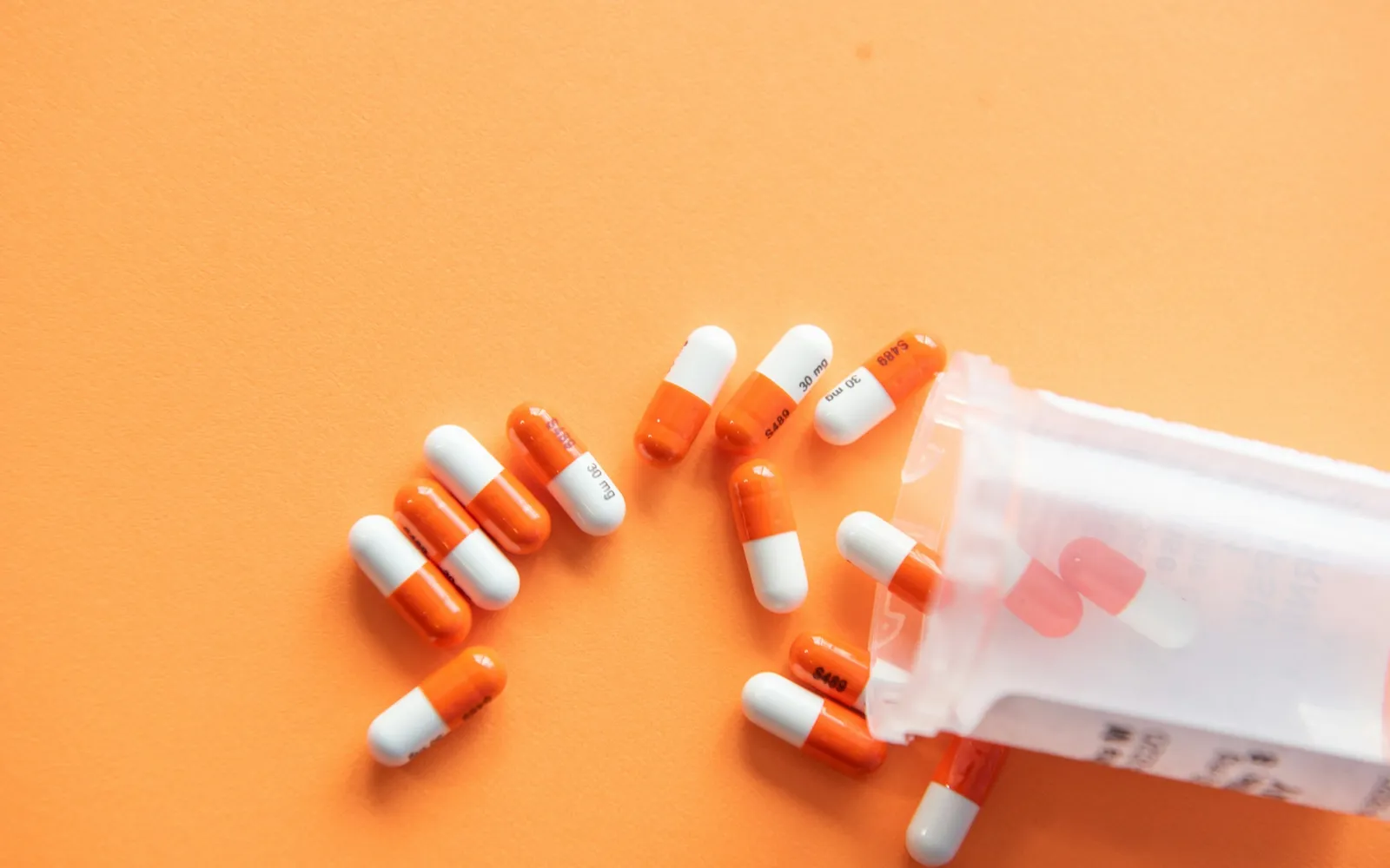 Orange and white capsules spilling from a prescription bottle on an orange background